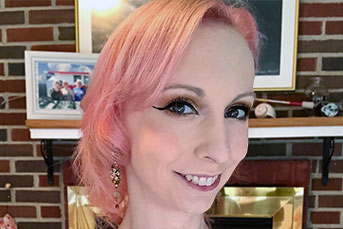 Headshot of Christie, a white cisgender woman with wavy shoulder length pink hair.