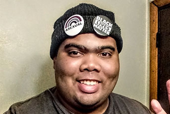 Headshot of Marshall, a Black man wearing a beanie with "Asexual" and "Black Lives Matter" pins on it.
